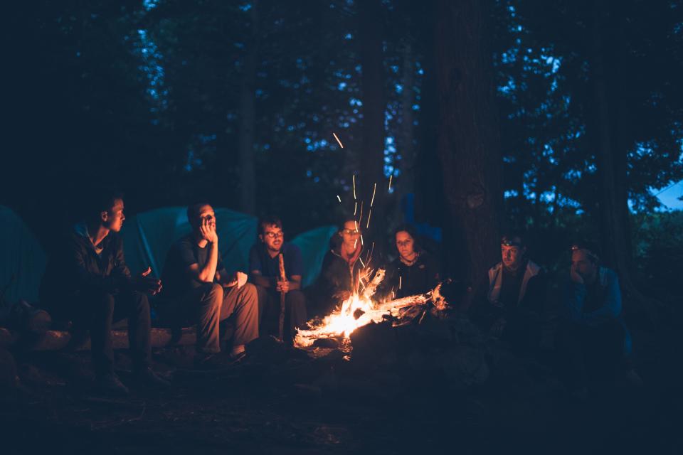Women in conversation around an outdoor fire at dusk